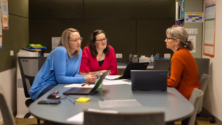 Three women sitting around a desk in an office environment.