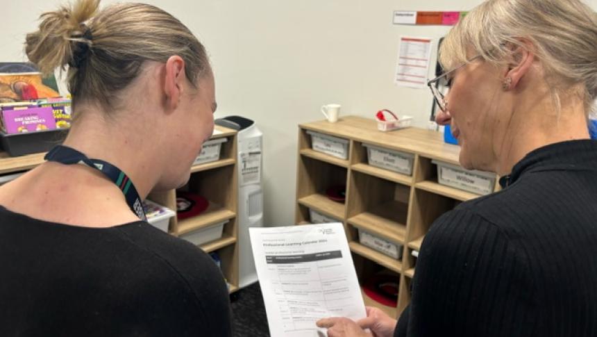 Two staff members look at a printed professional learning calendar.