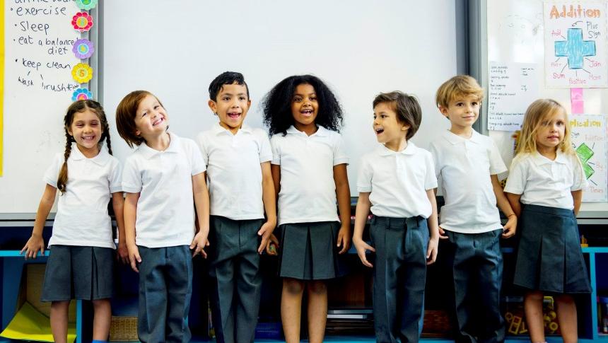 Group of happy primary school children standing in front of a whiteboard