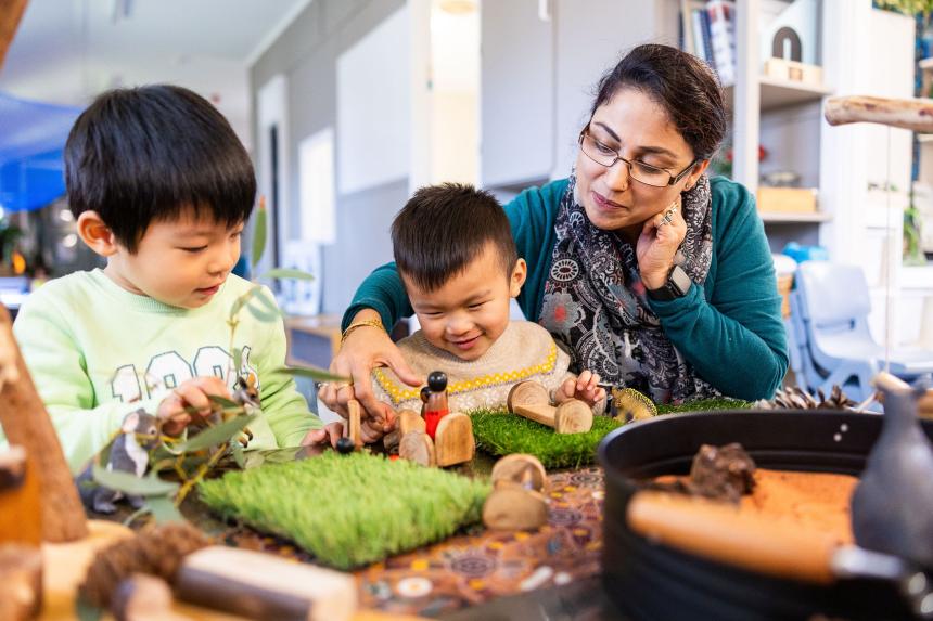 Two primary-school-aged children sit at a desk in a classroom. One is smiling and leafing through a workbook and the other is laughing.